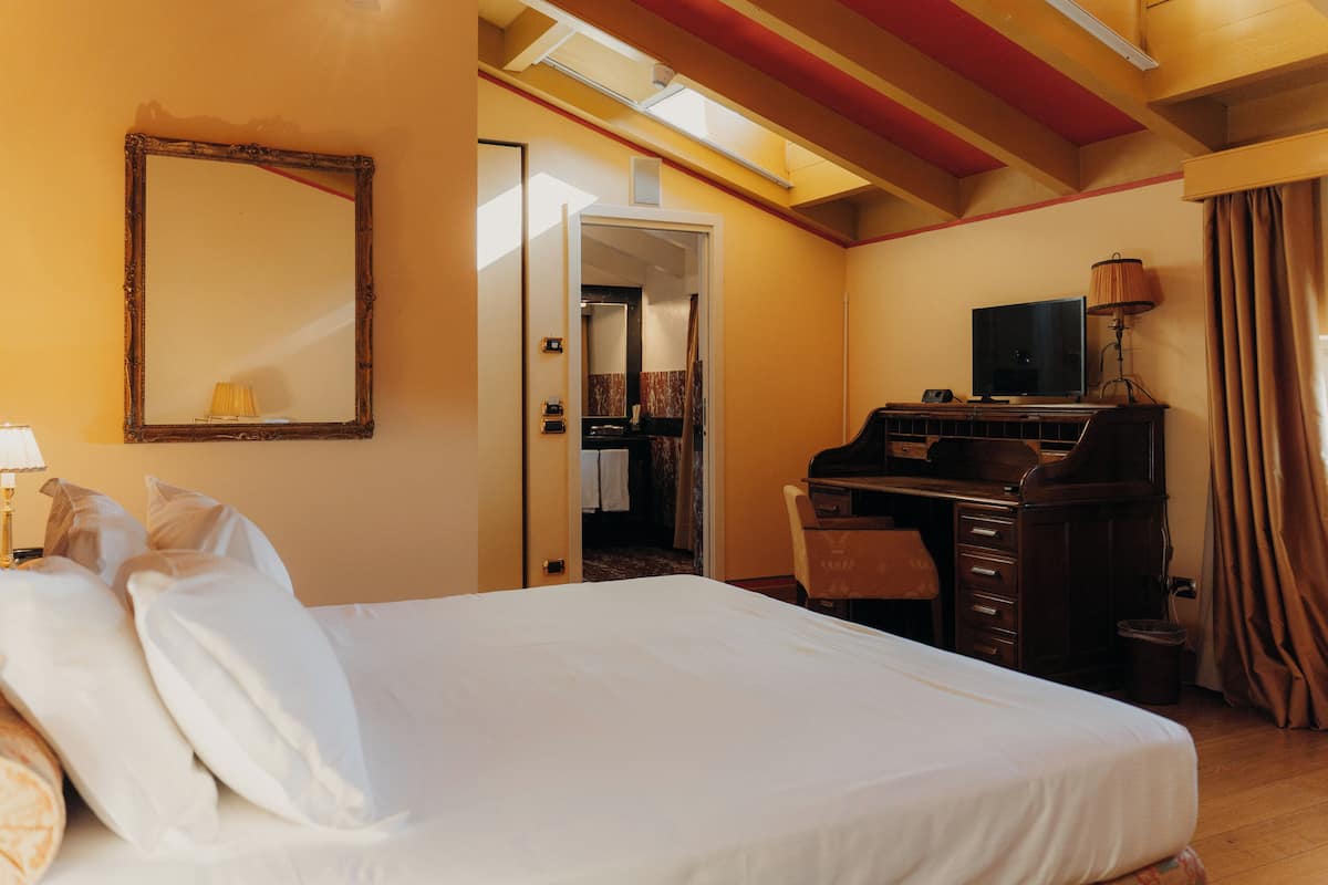 A hotel room with a large bed, a desk with a computer, a television, and a mirror on the wall.