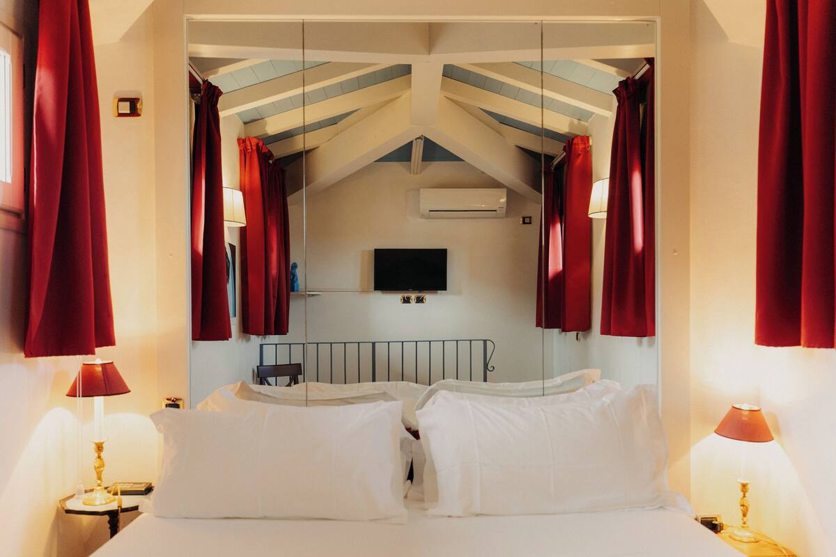 A hotel room with a bed, a TV mounted on the wall, and an air conditioning unit.