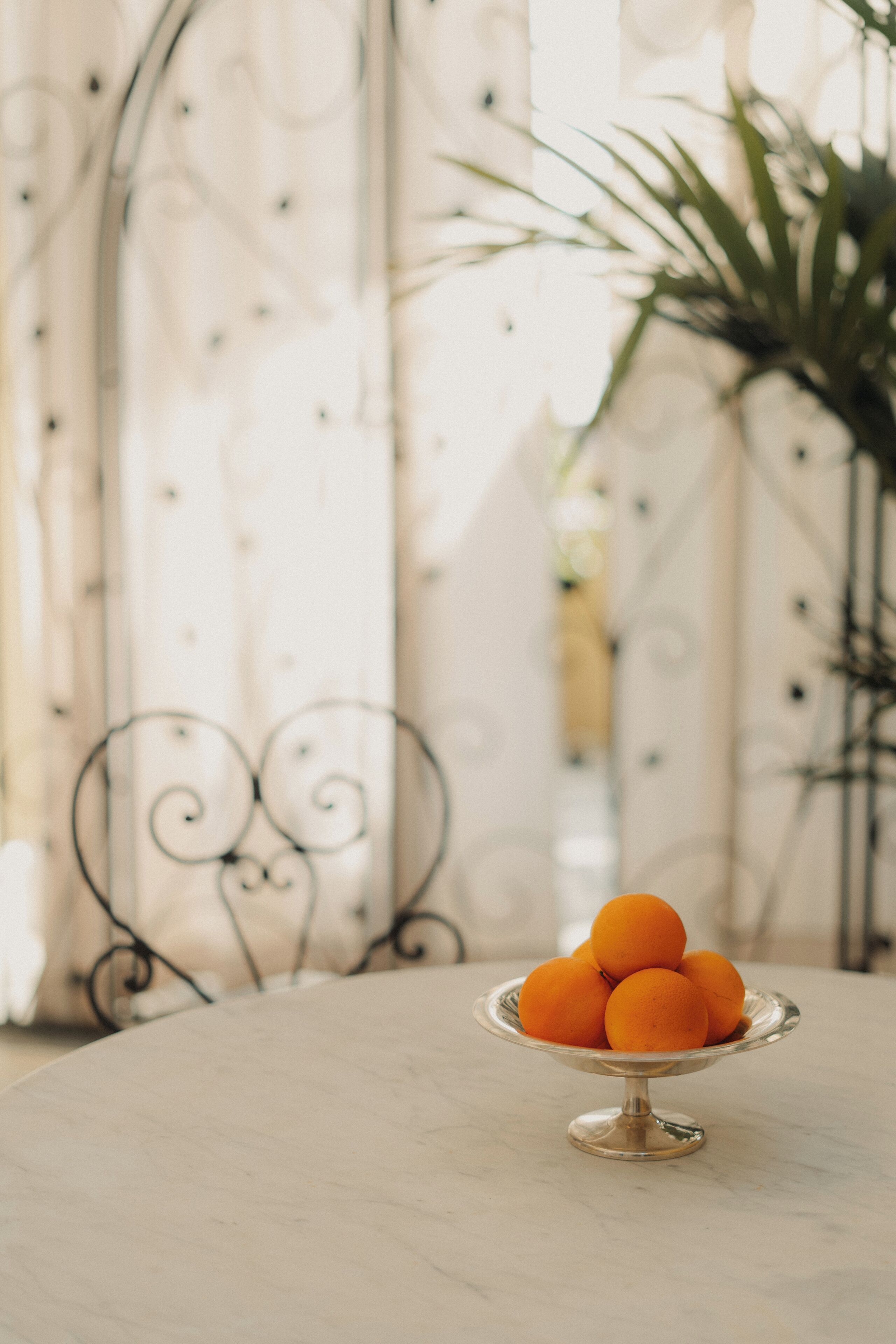 A table with a metal stand holding a bowl of oranges.