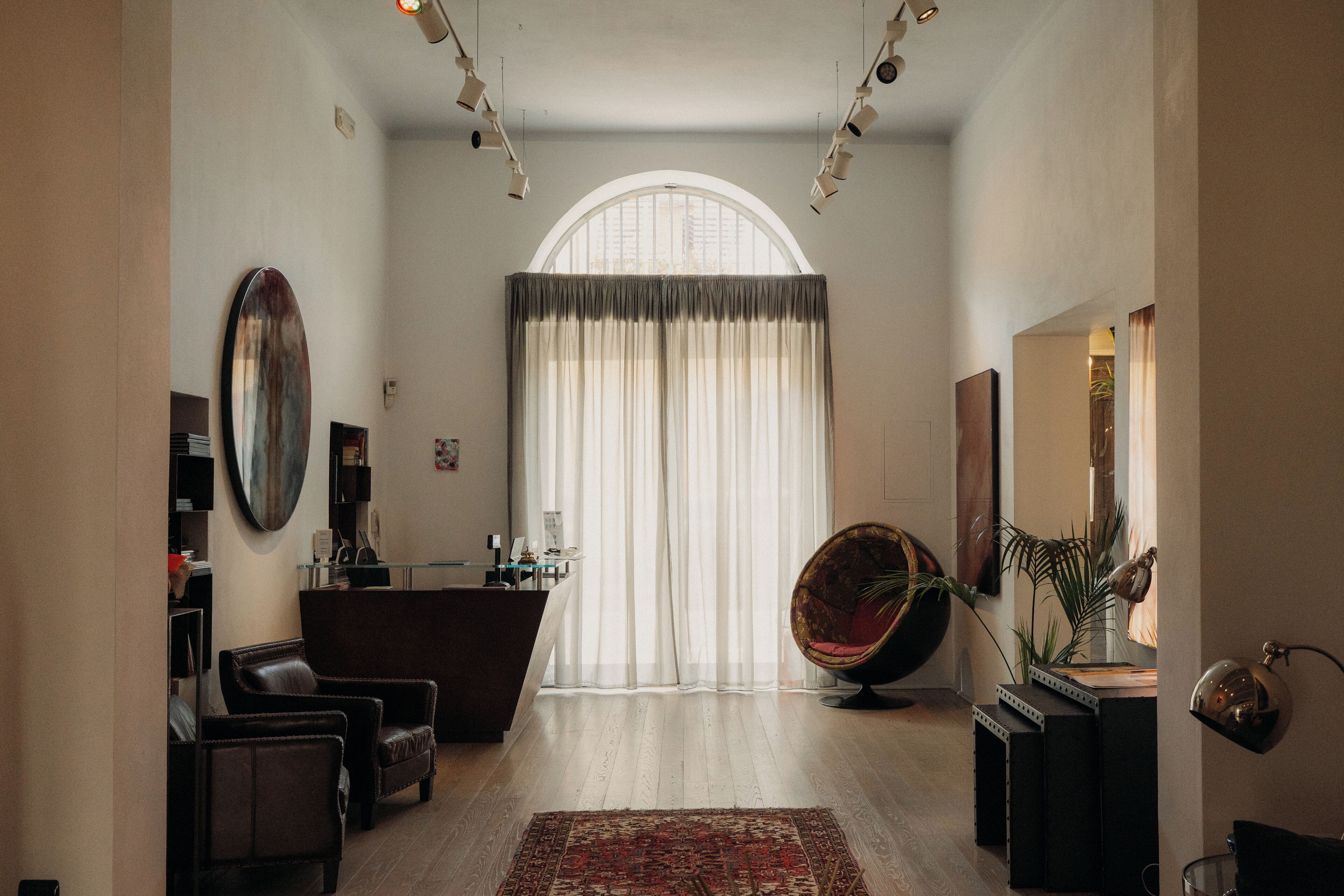 Un'ampia zona giorno con un'elegante finestra ad arco, divani in pelle, una poltrona rotonda e una piccola scrivania con lampada.