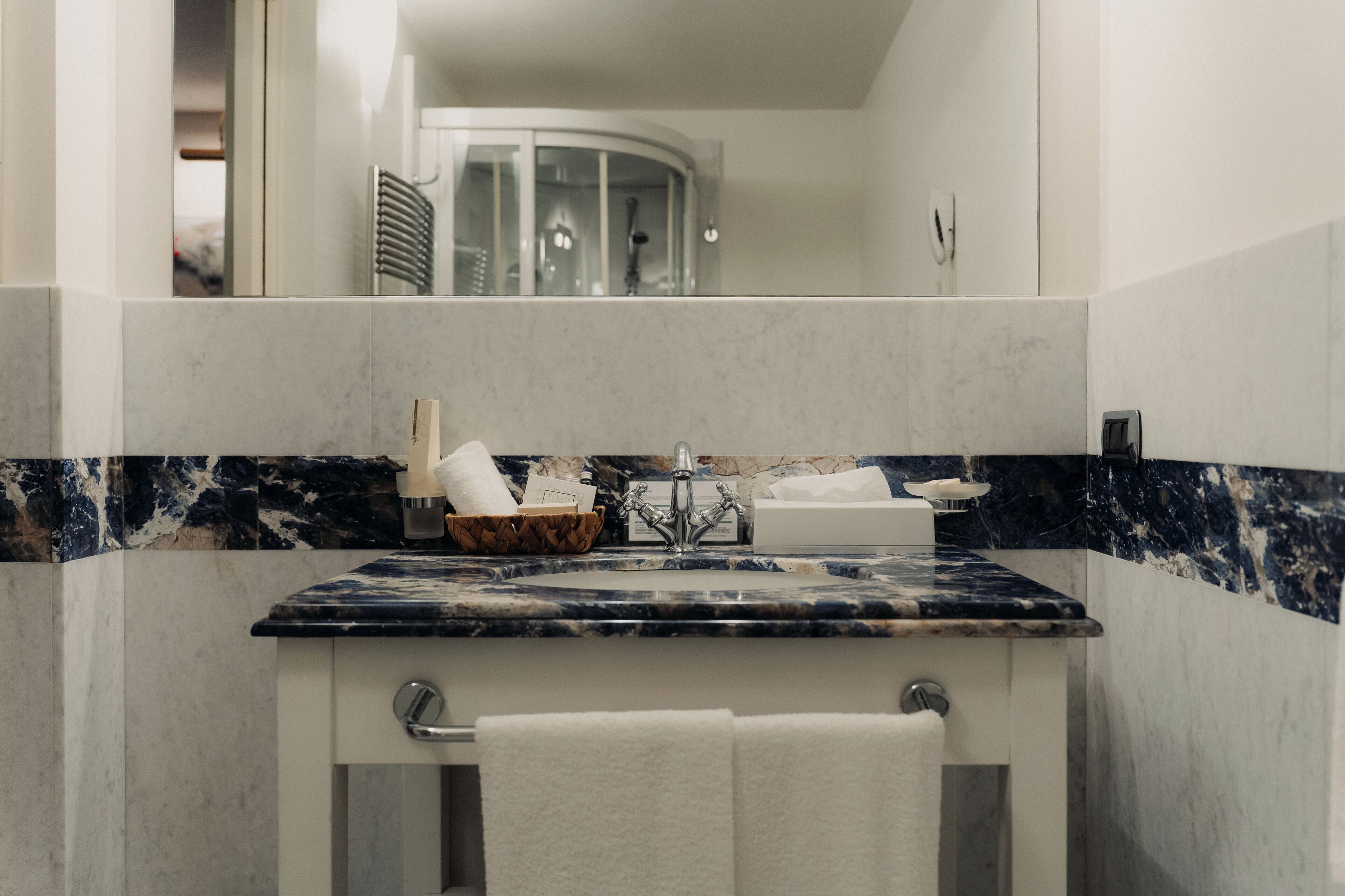 Un baño con lavamanos de mármol, un perchero y una cabina de ducha de vidrio.