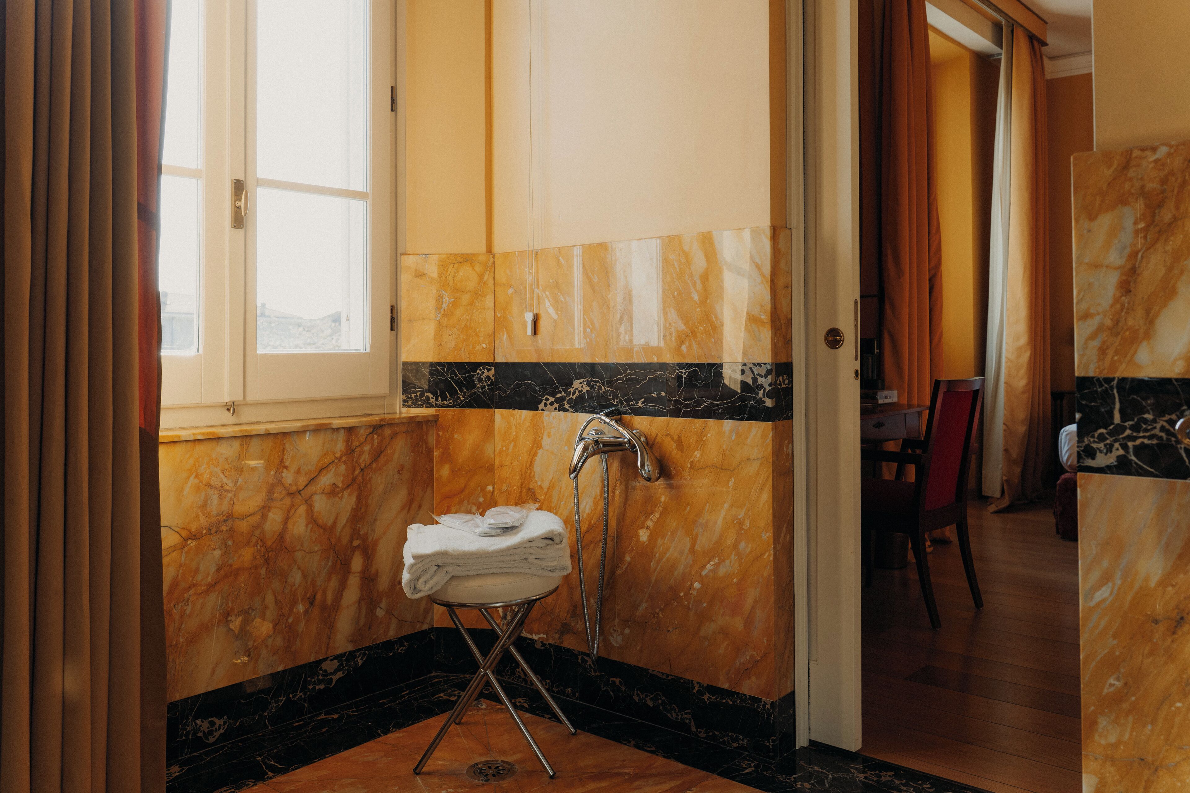 A bathroom with a marble wall, a towel rack, and a shower.