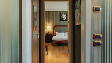Una habitación de hotel con una cama, una mesita de noche, una lámpara y un taburete rojo.