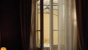 A hotel room with a bed, a nightstand with a lamp, and a view of an outdoor balcony with a table and chairs.
