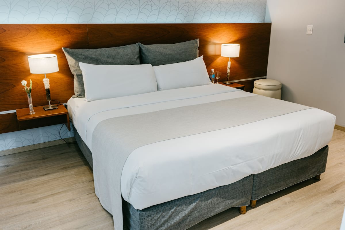 A neatly made bed with white linens, two bedside lamps, and a wooden headboard.