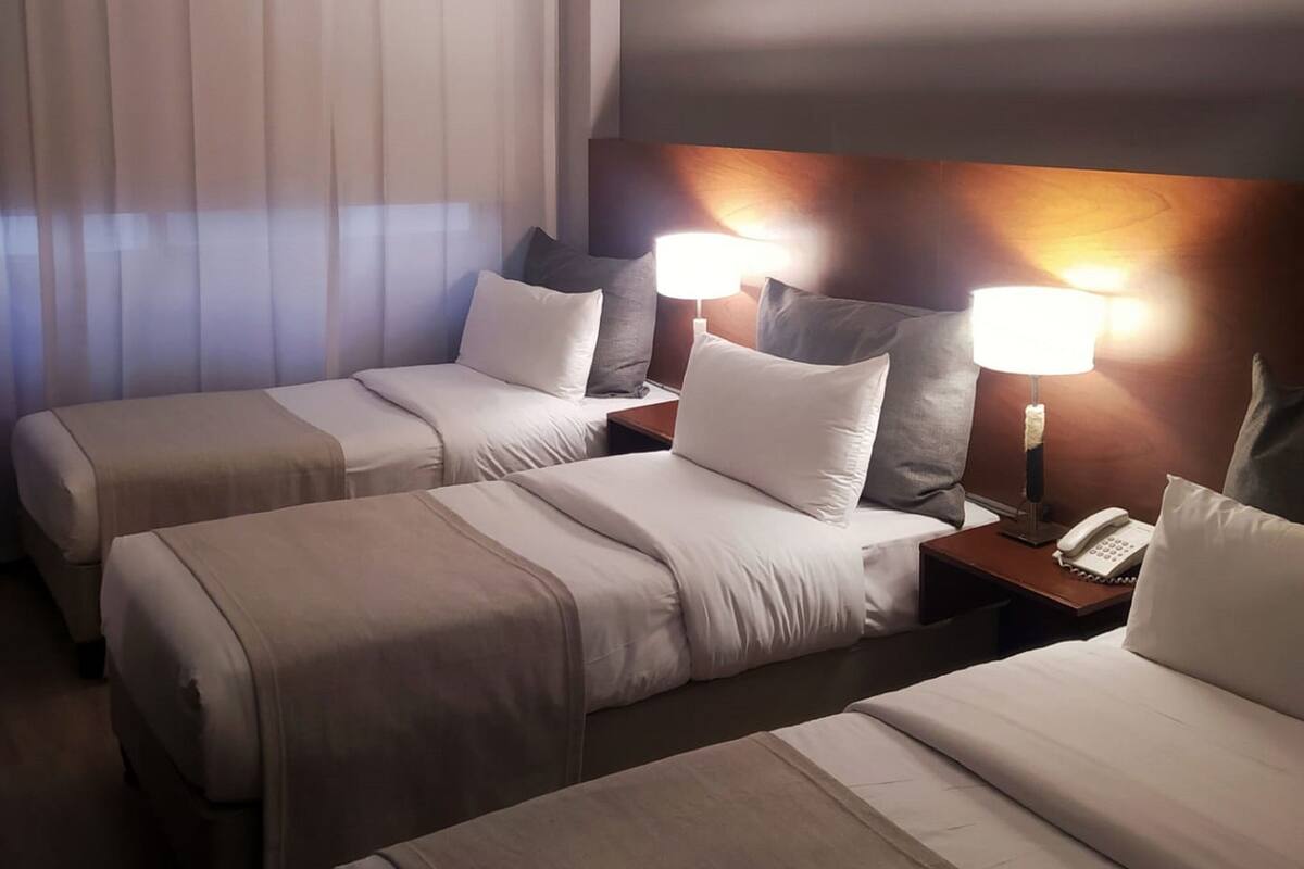 A hotel room with two beds, a nightstand with a phone, and a wall-mounted lamp.