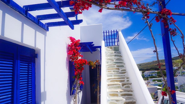 A white building with blue shutters and a stone staircase leading to a door.