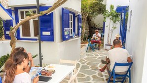 A courtyard with a white table and blue chairs, surrounded by buildings with blue shutters and a stone floor.