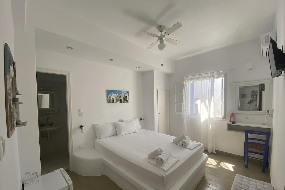 A bedroom with a bed, a ceiling fan, a window with curtains, a bedside table, and a mirror.