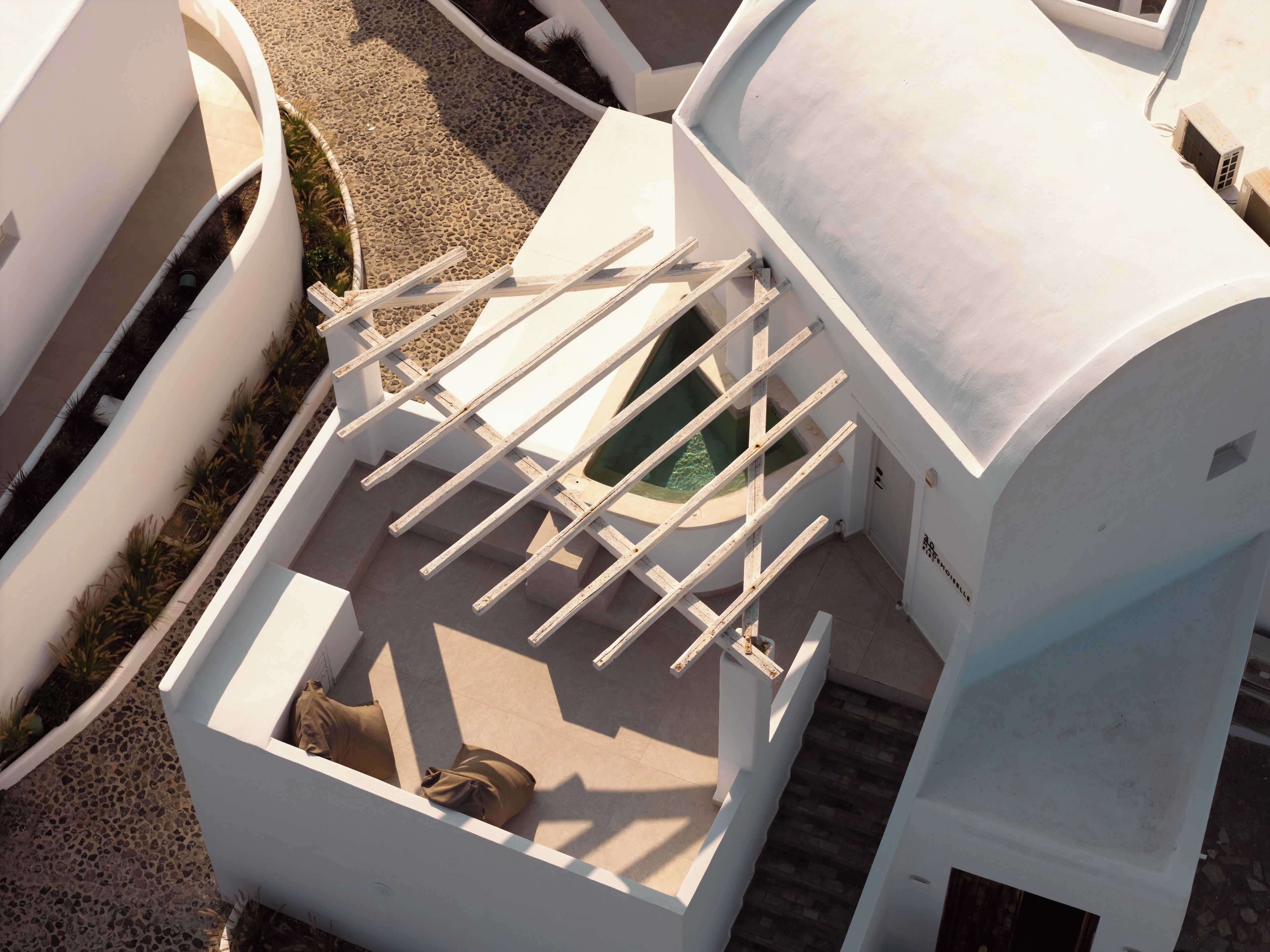 A modern building with a white exterior, a covered outdoor seating area with a pool, and a staircase leading to an upper level.