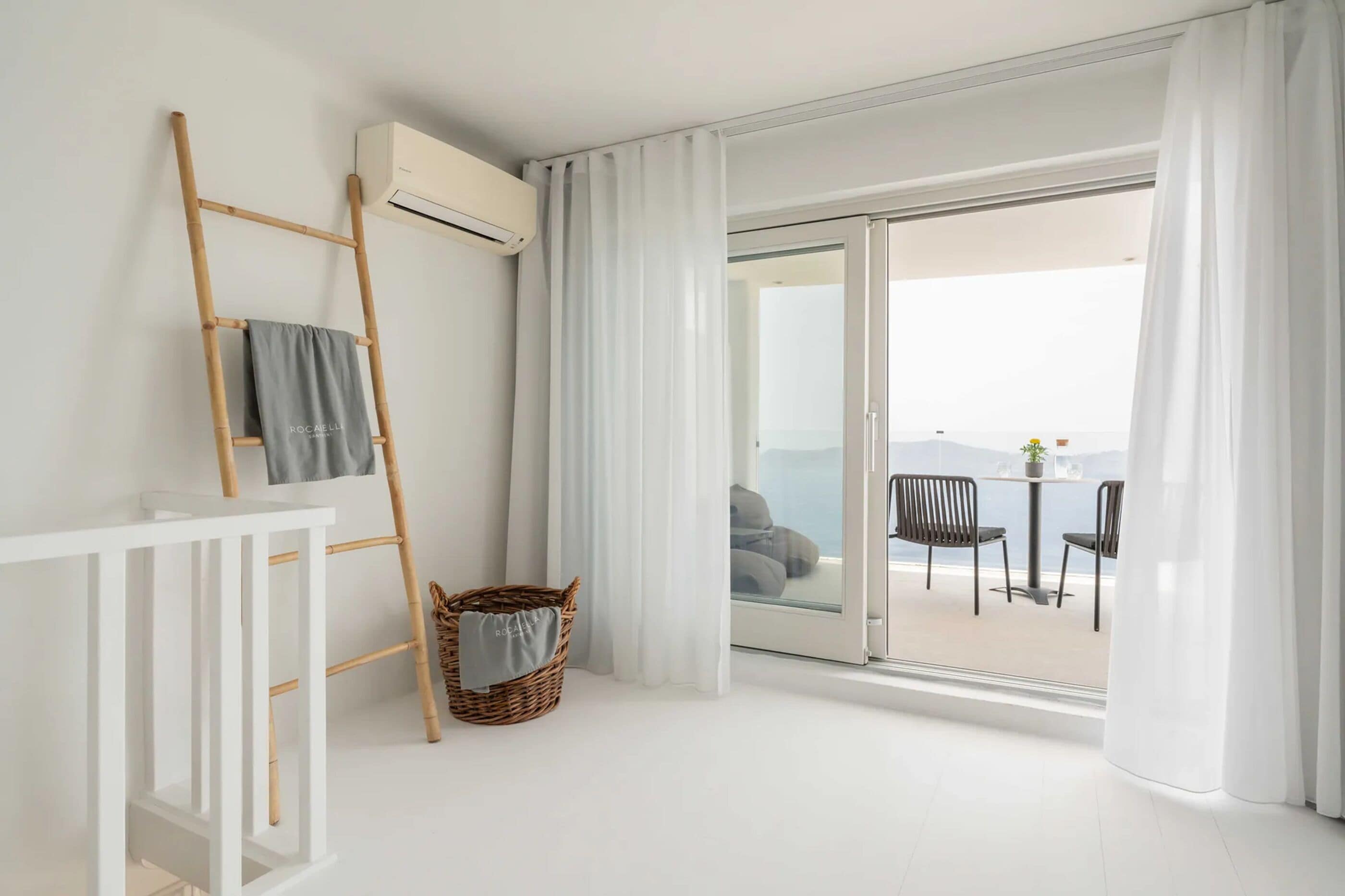 Una habitación moderna con barandilla blanca, una escalera de bambú, una cesta de mimbre y vista al mar a través de un vidrio.