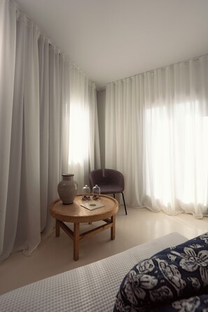 A room with a round wooden table, a chair, a vase, and a bed with a patterned blanket.