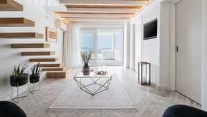 Un salon moderne avec une table basse en verre, des étagères en bois et une vue sur l’extérieur.
