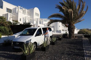 A white car parked in front of a white building with a palm tree nearby.
