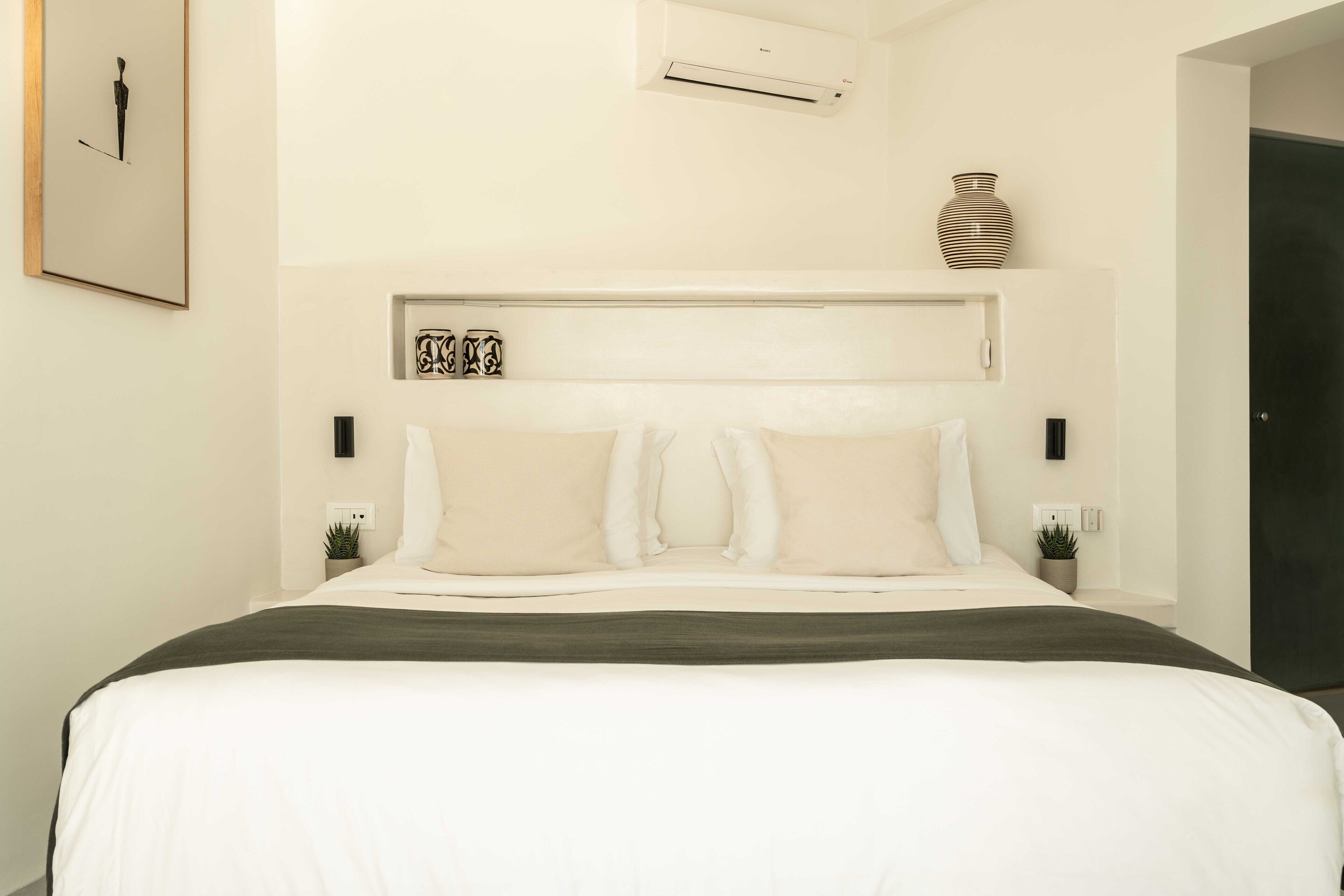Un dormitorio moderno con una cama grande, cabecera con almacenamiento, mesitas de noche con plantas y aire acondicionado instalado en la pared.