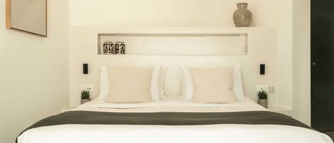 Un dormitorio moderno con una cama grande, cabecera con almacenamiento, mesitas de noche con plantas y aire acondicionado instalado en la pared.