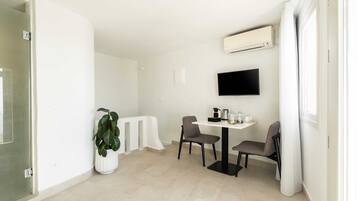 Una habitación moderna y luminosa con una mesa de comedor, dos sillas, una planta en maceta, un televisor de pantalla plana montado en la pared y un equipo de aire acondicionado.