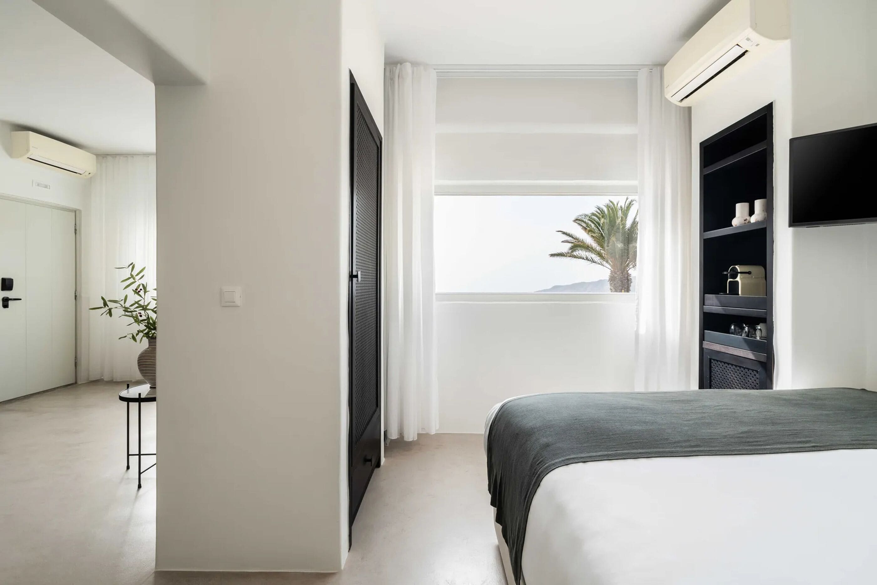 A modern hotel room with a bed, a TV, a small table with a plant, and a view of the sea.