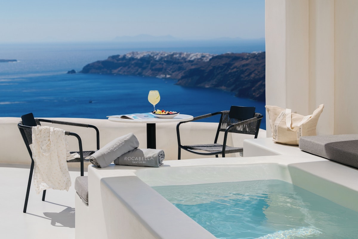 A balcony with a view of the sea, a table with a glass of wine, and a hot tub.