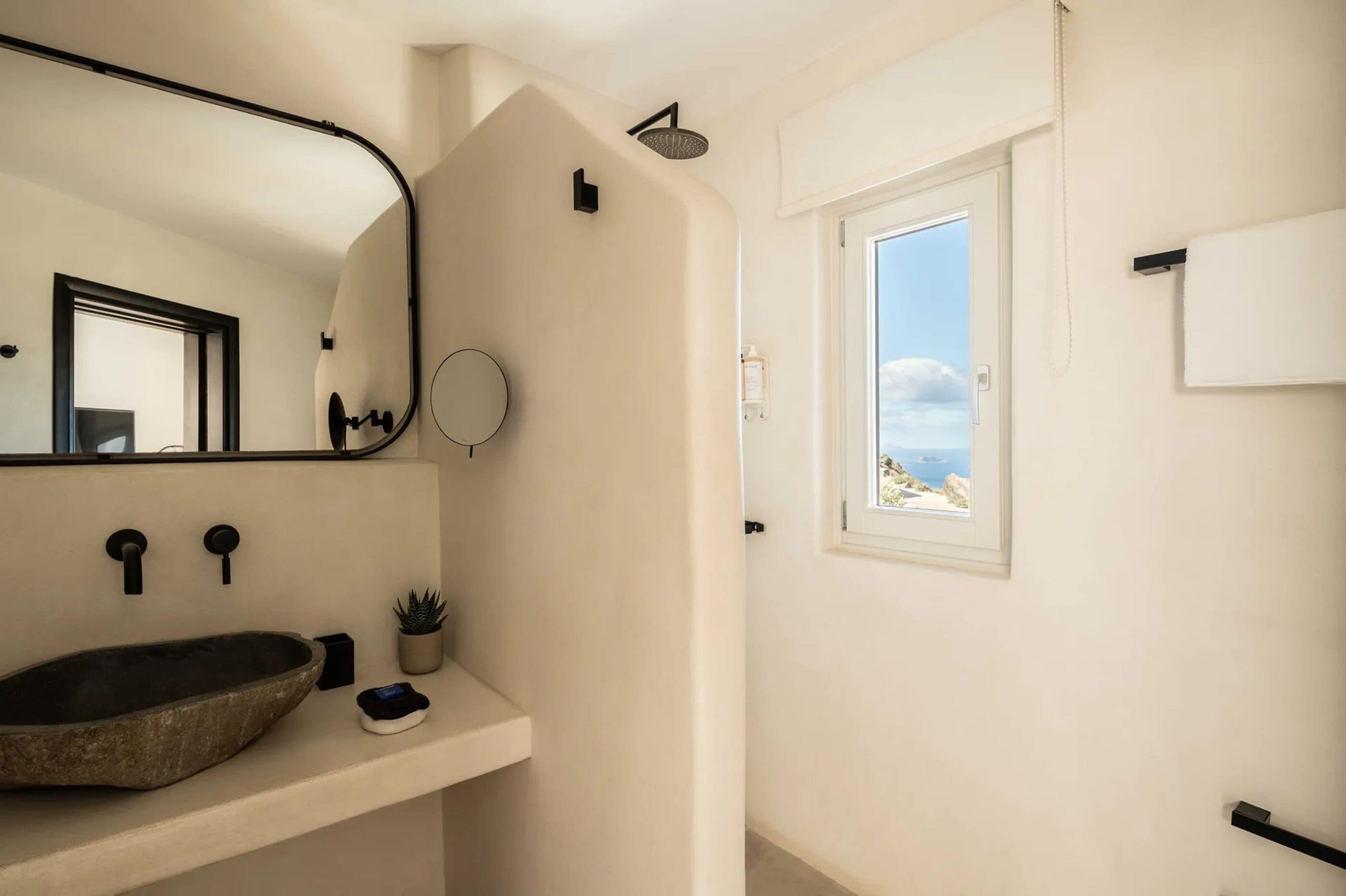 A modern bathroom with a large mirror, a vessel sink, a shower, and a window with a view of the sea.
