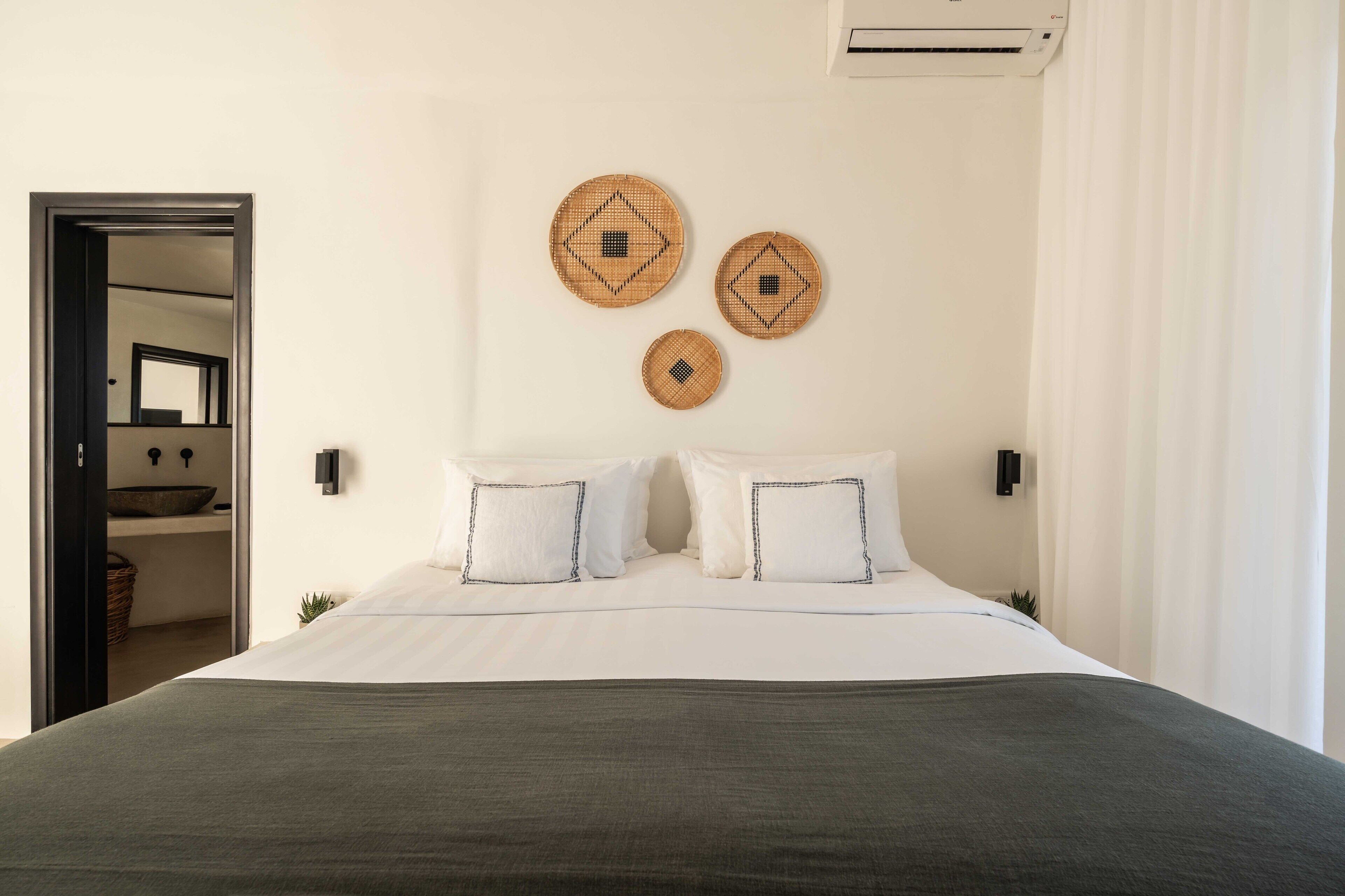 A bedroom with a large bed, two wall-mounted decorative items, and a visible bathroom door.