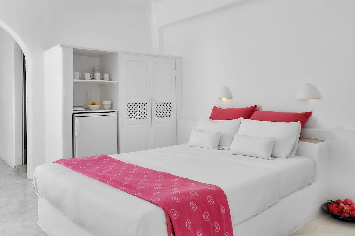 A white room with a bed, a wardrobe, and a small kitchen area.