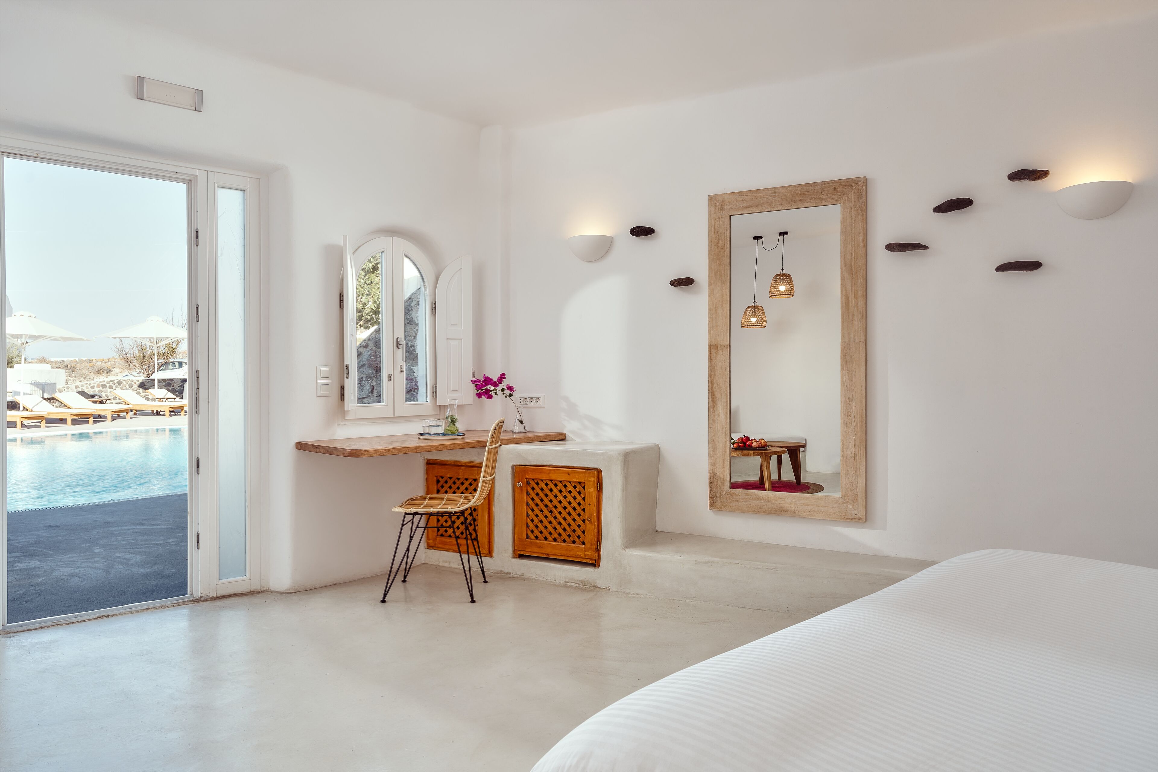 Ein modernes Hotelzimmer mit einem großen Bett, einem Schreibtisch mit Stuhl, einem großen Spiegel und Blick auf einen Pool.