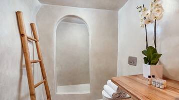 Un baño con una escalera de madera, un lavabo blanco con artículos de aseo y una orquídea en maceta.