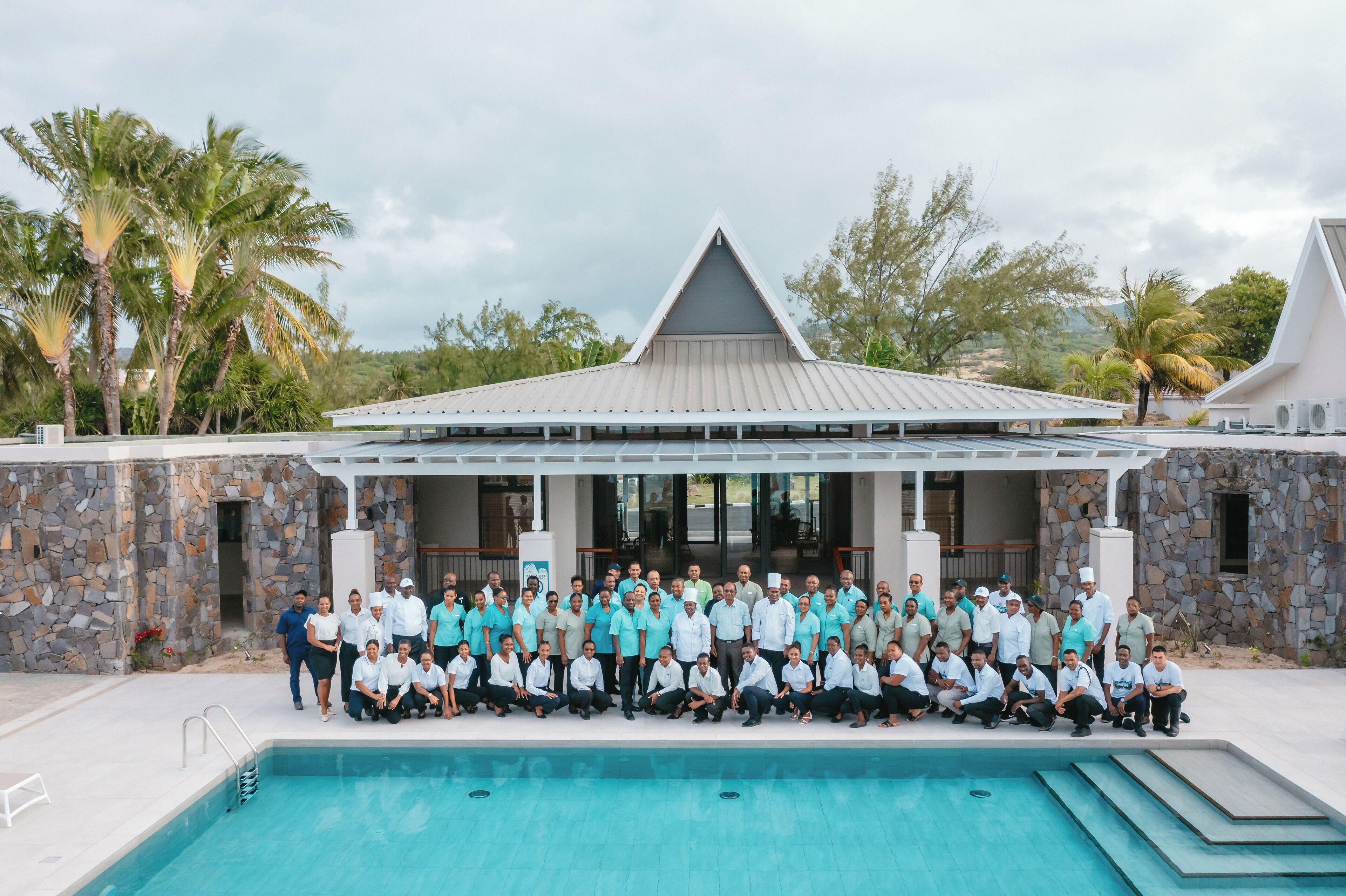 Un grupo de personas posando frente a una piscina, con un edificio de piedra al fondo.
