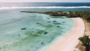En vy över en strand från ovan, med flera båtar som ligger ankrade nära stranden och en tydlig utsikt över havet.