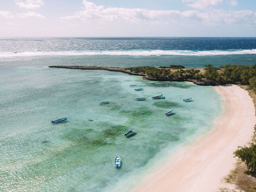 Luchtbeeld van een strand met verschillende boten die bij de kust liggen aangemeerd en een helder uitzicht over de oceaan.
