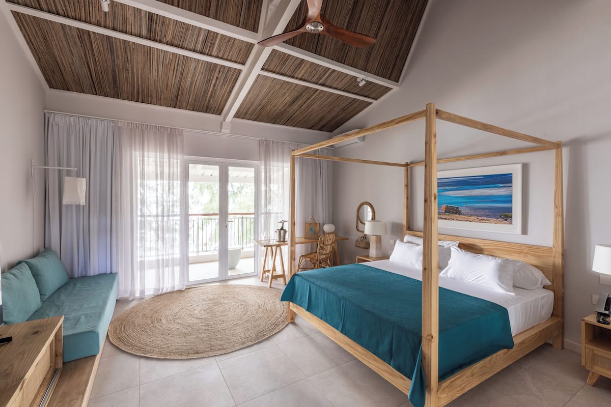 A spacious bedroom with a four-poster bed, a sofa, a dining table, and a balcony with curtains.