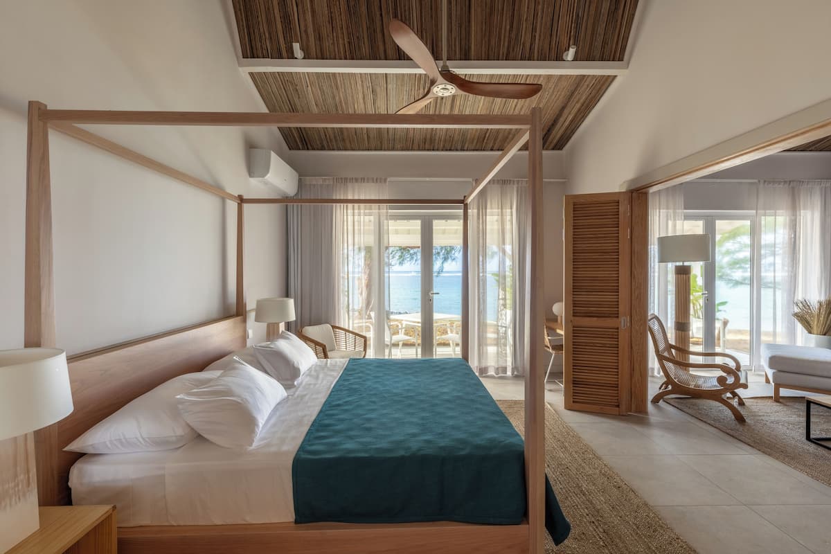 A spacious bedroom with a large bed, a ceiling fan, and a view of the sea through the glass doors.