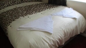 Ein Bett mit kariertem Kopfteil, weißer Bettwäsche und einem gefalteten weißen Handtuch.