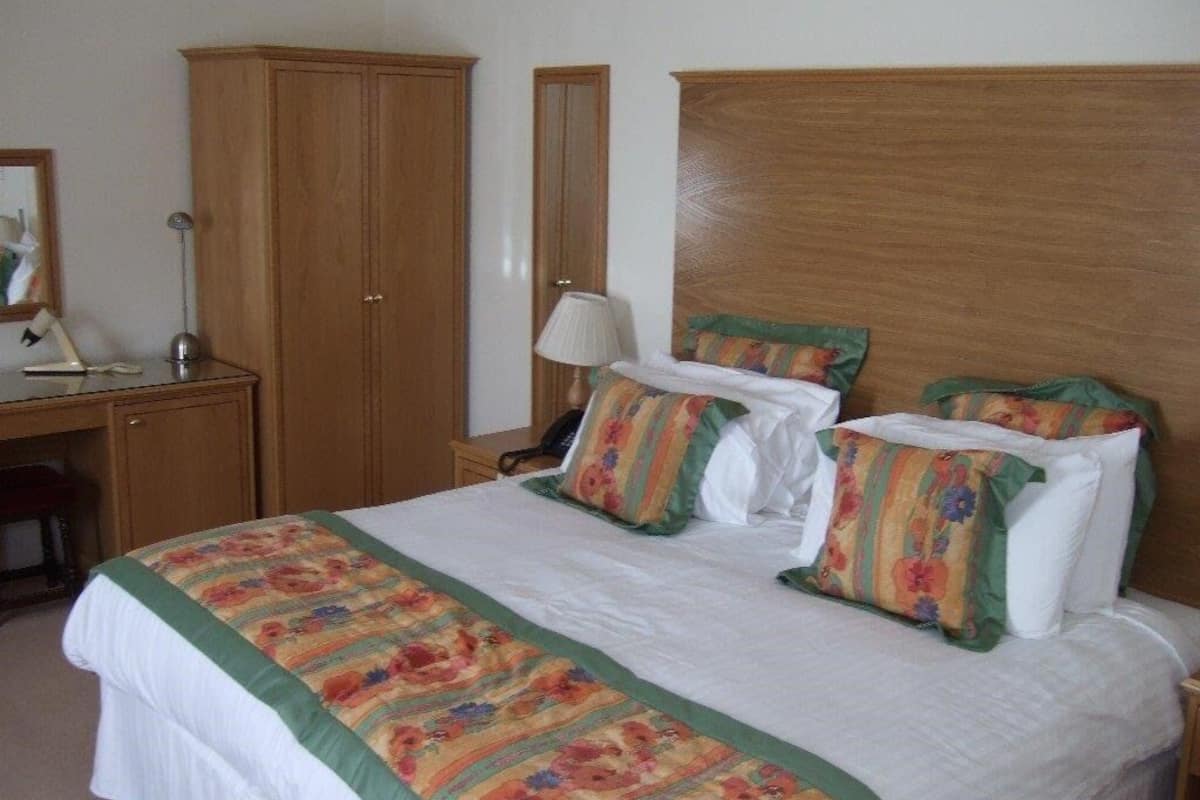 Quarto com cama grande, guarda-roupa de madeira, escrivaninha com luminária e uma cadeira.
