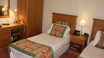 Quarto de hotel com duas camas de solteiro, guarda-roupa de madeira, escrivaninha com cadeira, mesa de cabeceira com abajur e telefone.
