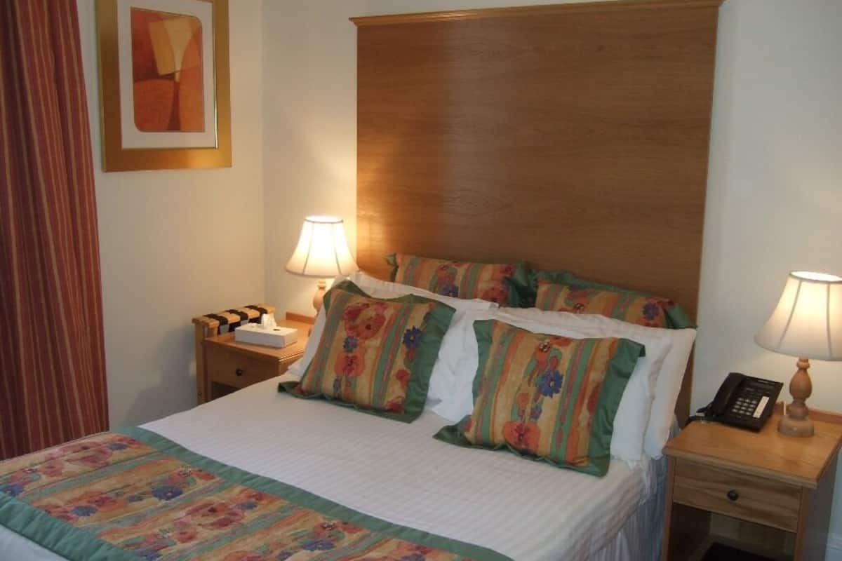 Cama bem arrumada com roupa de cama floral, duas mesas de cabeceira com abajures e uma cabeceira de madeira.
