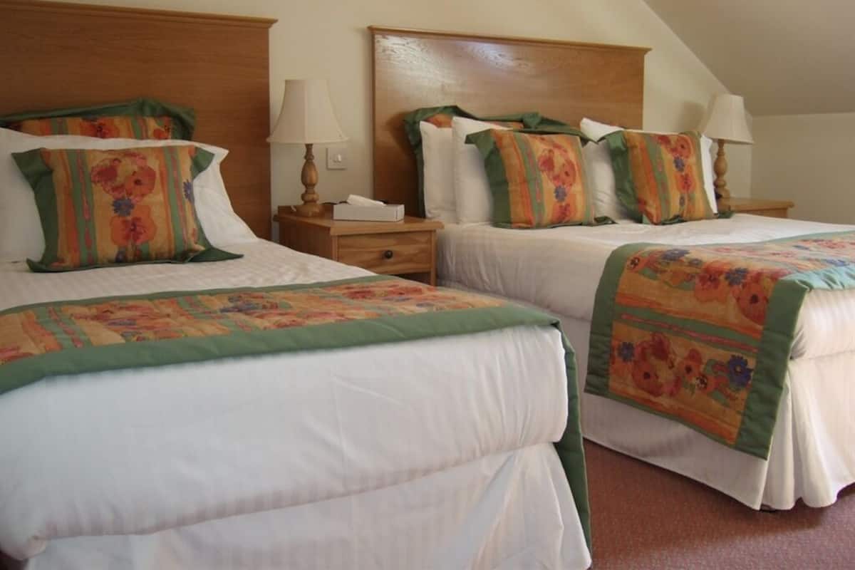Quarto com duas camas, cada uma com roupa de cama estampada com flores e detalhes em verde. Há mesas de cabeceira com abajures e um porta-lenços.