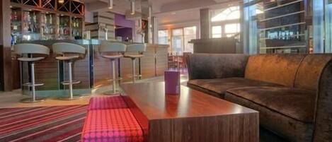 A modern bar area with a wooden counter, two bar stools, and a leather couch.