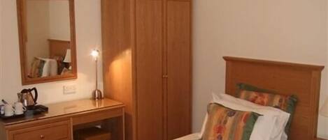 A bedroom with a bed, a wooden wardrobe, a bedside table, a mirror, and a desk with a lamp.