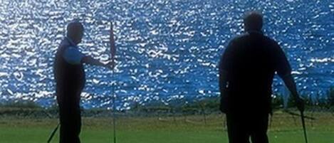 A golf course with a view of the ocean and a large dome structure in the background.