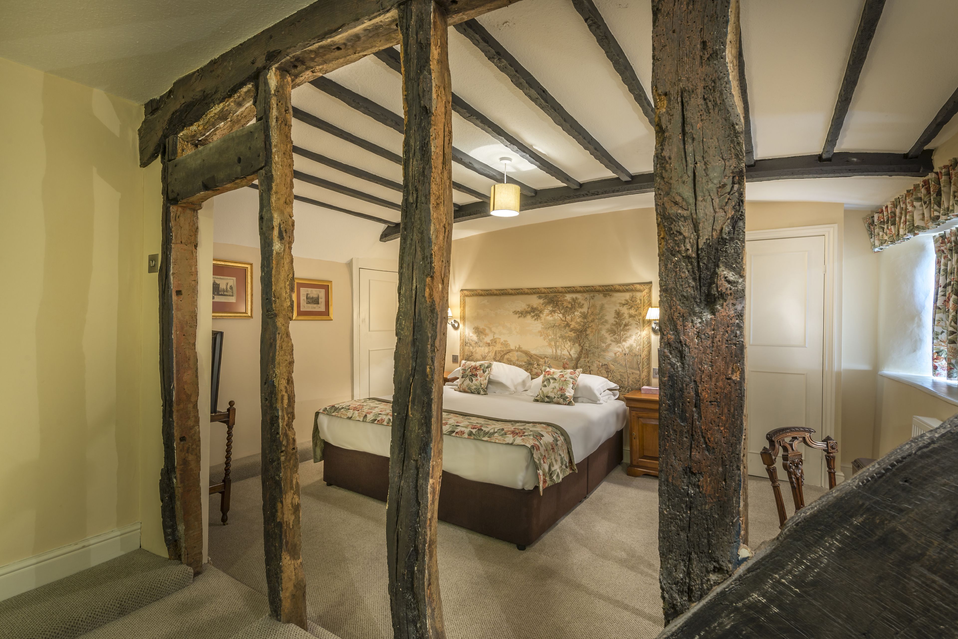 Un dormitorio con una cama grande, vigas de madera, piso alfombrado y una mesita de noche.