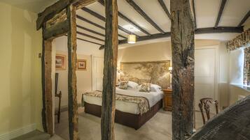 Un dormitorio con una cama grande, vigas de madera, piso alfombrado y una mesita de noche.