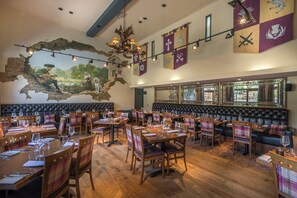 Un restaurante con mesas y sillas de madera, un mural en la pared y una lámpara de cristal.