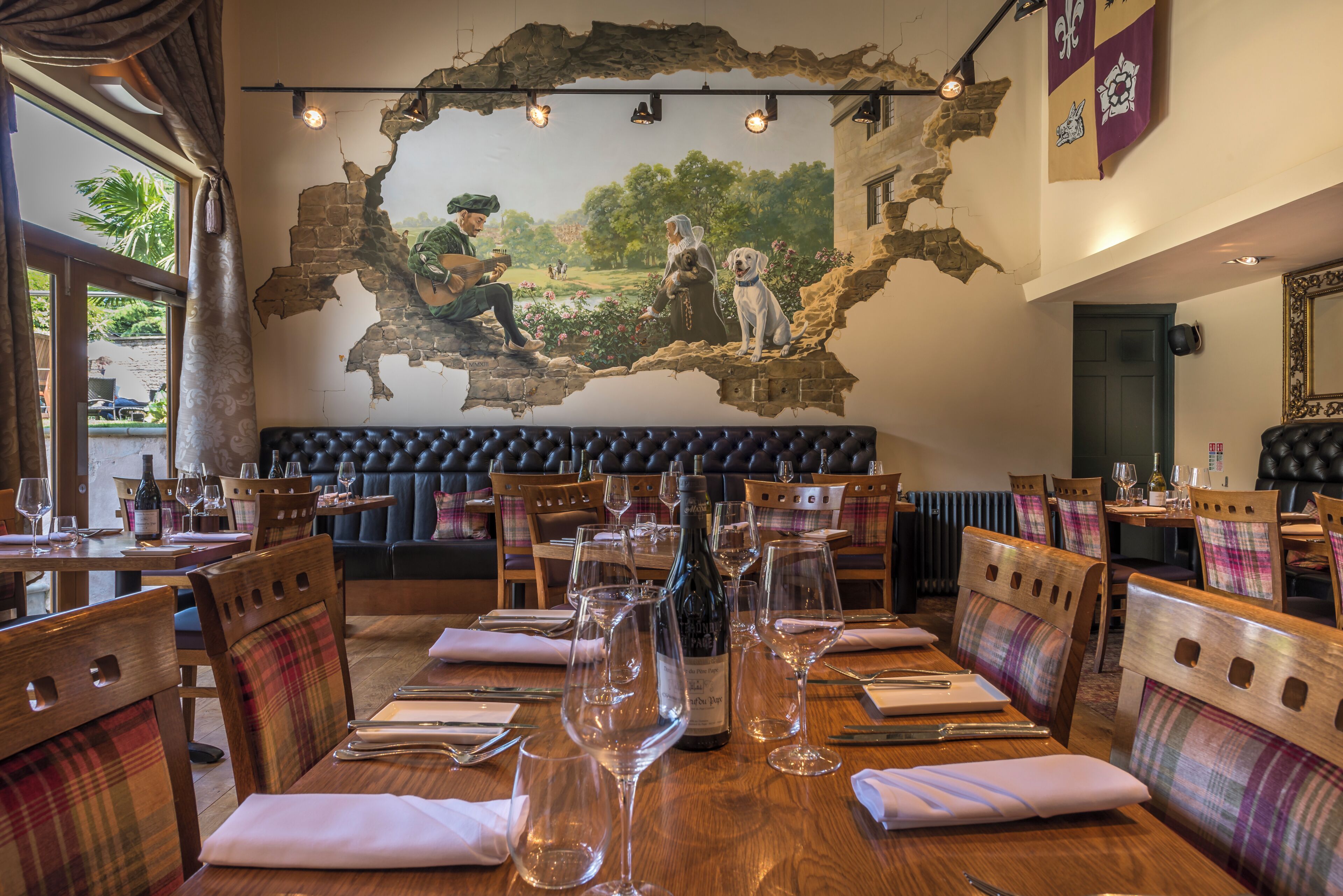 A restaurant with wooden tables, plaid chairs, and a mural on the wall.