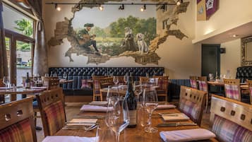 A restaurant with wooden tables, plaid chairs, and a mural on the wall.
