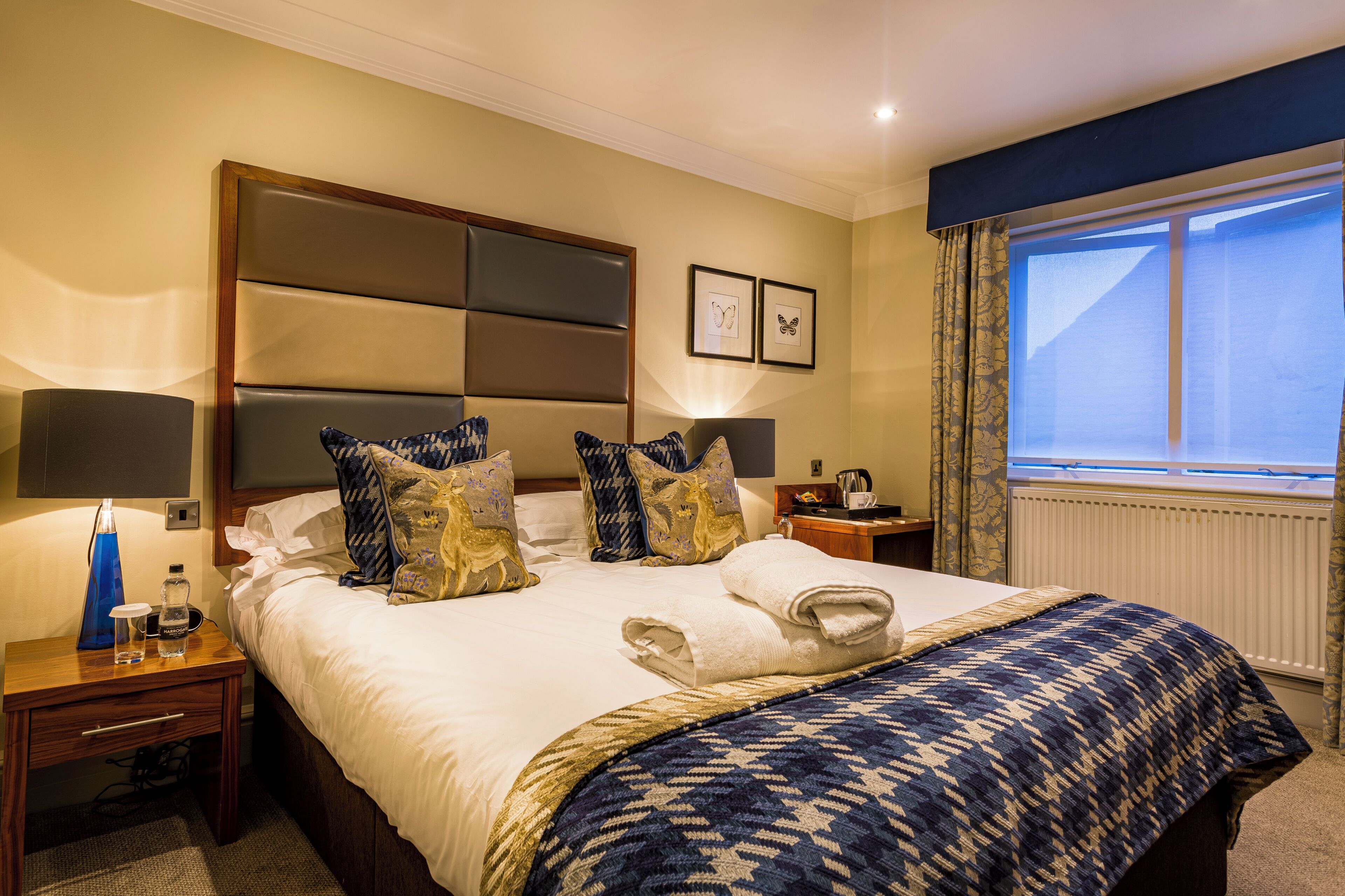 A hotel room with a large bed, two bedside tables, a window with curtains, and a wall-mounted picture.