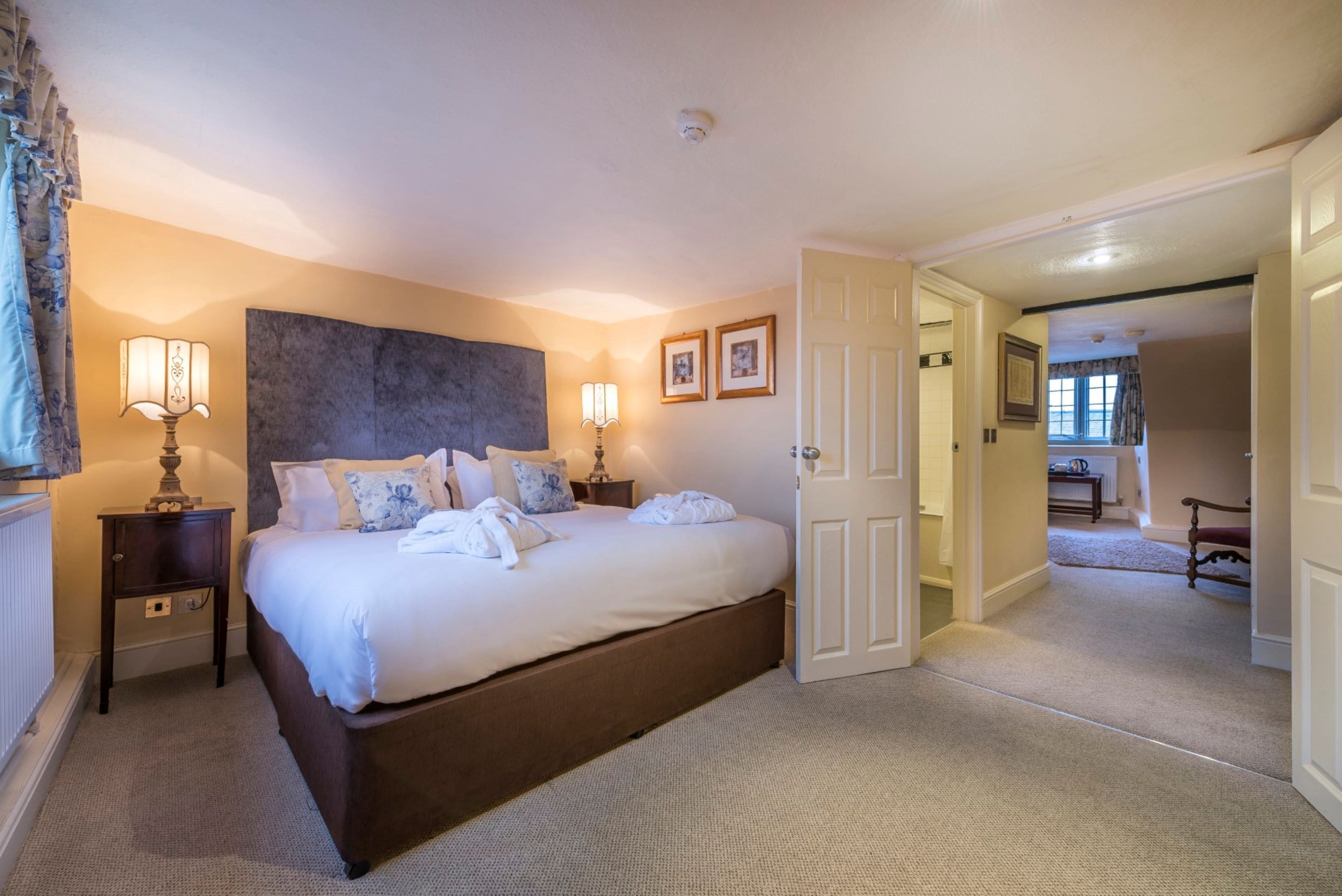 A bedroom with a large bed, two bedside tables, a headboard, and a door leading to another room.