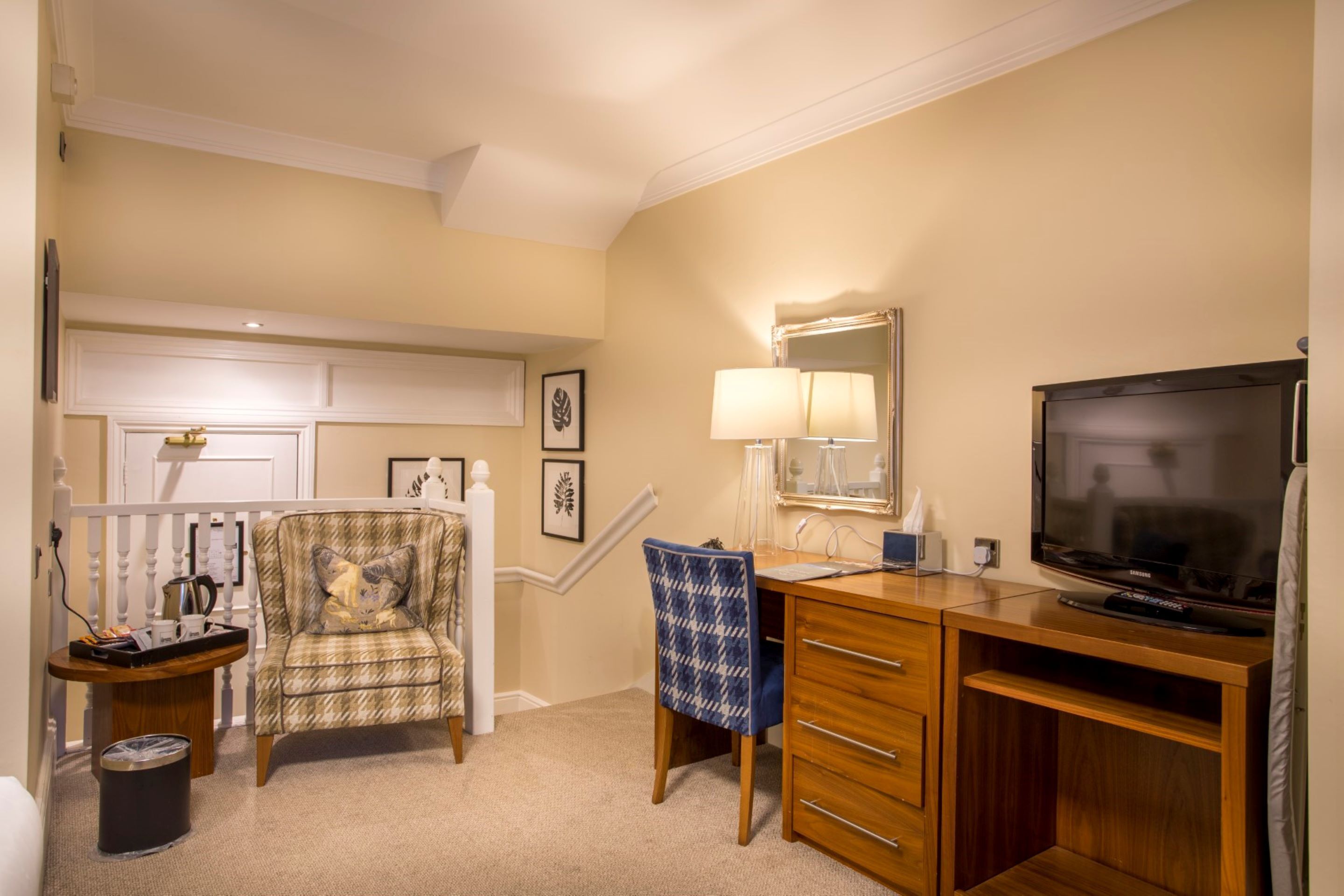 A hotel room with a wooden desk, a television, a chair, a lamp, and a trash can.