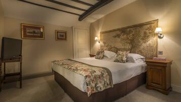 A bedroom with a large bed, wooden headboard, two wall-mounted lamps, a TV on a stand, and framed pictures on the wall.
